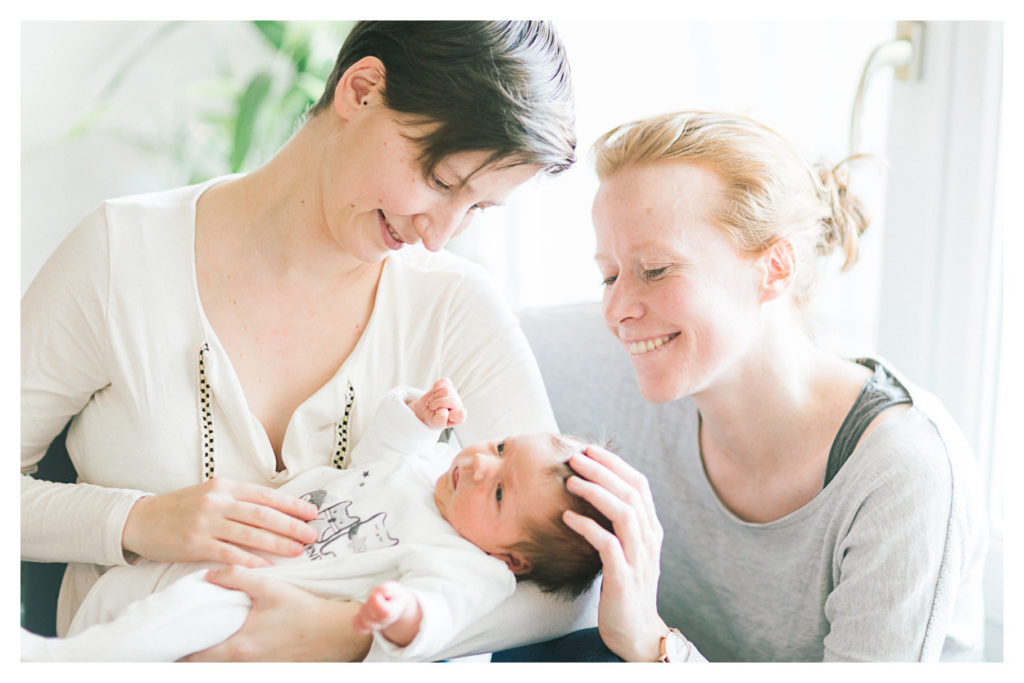 Photographe bébé à Genève en Suisse. Deuxièmement, photo du couple de maman qui porte leur fille dans les bras lors du shooting photo de la séance naissance